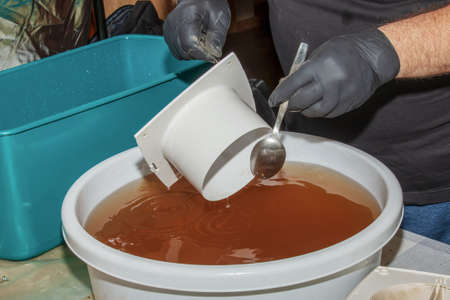 Washing the plastic parts of a very dirty kitchen exhaust fan in an aqueous solution of sodium hydroxide. A man works in protective gloves and thoroughly rinses the details.の写真素材