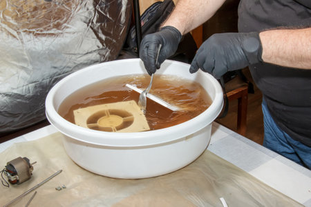Washing the plastic parts of a very dirty kitchen exhaust fan in an aqueous solution of sodium hydroxide. A man works in protective gloves and thoroughly rinses the details.の写真素材