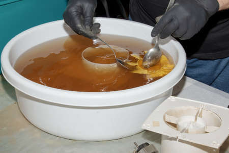 Washing the plastic parts of a very dirty kitchen exhaust fan in an aqueous solution of sodium hydroxide. A man works in protective gloves and thoroughly rinses the details.の写真素材