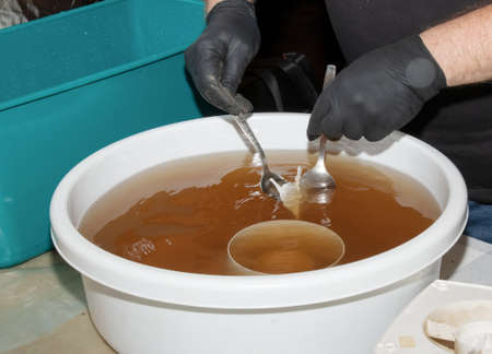 Washing the plastic parts of a very dirty kitchen exhaust fan in an aqueous solution of sodium hydroxide. A man works in protective gloves and thoroughly rinses the details.の写真素材