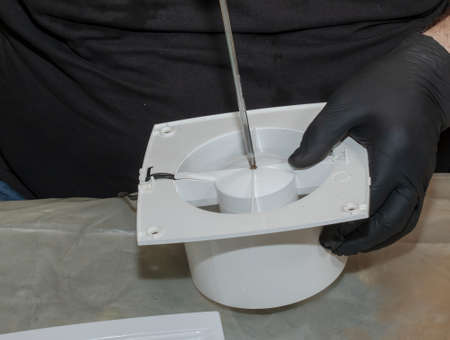 The process of assembling the kitchen exhaust fan after cleaning the wash. A man works with a screwdriver in his hands.の写真素材