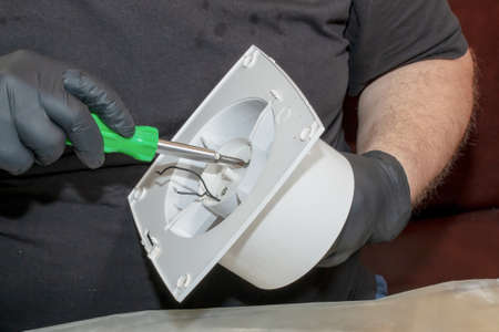 The process of assembling the kitchen exhaust fan after cleaning the wash. A man works with a screwdriver in his hands.の写真素材