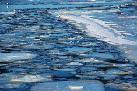 Winter nature background with blocks of ice on frozen water in spring. Abstract background of...