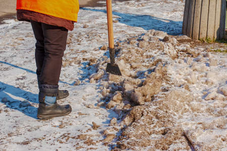 A woman worker cleans the ice and removes snow from paving slabs using an icebreaker. A man breaks ice with a steel blade crusher, an ice-breaking tool. The janitor cleans up the area.の写真素材