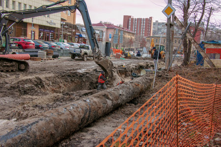 Dnipropetrovsk, Ukraine - 11.30.2021: Construction work on laying sewer pipes in urban areas. Tractor and excavator work.のeditorial素材