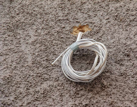 Thick twisted white wire sticking out of the wall. A coil of electrical cable on a gray wall.の写真素材