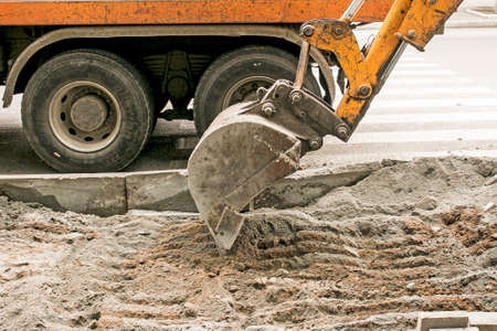 Road works on the city street. The excavator bucket collects the old pavement and loads it into a dump truck.の写真素材