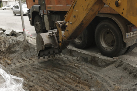 Dnepropetrovsk, Ukraine - 09.24.2021: Road works on the city street. The excavator bucket collects the old pavement and loads it into a dump truck.のeditorial素材