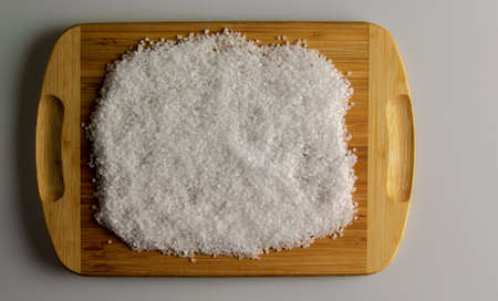 Background of coarsely ground salt on a wooden kitchen board. Texture of sea salt for food seasoning.の写真素材