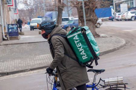Dnepropetrovsk, Ukraine - 02.07.2022: A delivery service courier with a thermal bag on a bicycle rides around the city. home food delivery.のeditorial素材