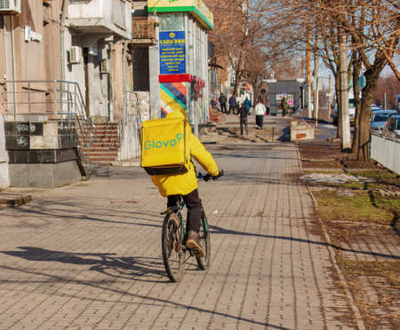 Dnepropetrovsk, Ukraine - 09/02/2022: A delivery service courier with a thermal bag on a bicycle rides around the city. home food delivery.のeditorial素材