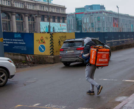 Dnepropetrovsk, Ukraine - 02.10.2022: A delivery service courier with a thermal bag walks through the city. home food delivery.のeditorial素材