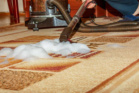 The process of cleaning the carpet with a vacuum cleaner with a water filter. A woman collects the remains of cleaning foam from the dirty surface of the carpet.の写真素材