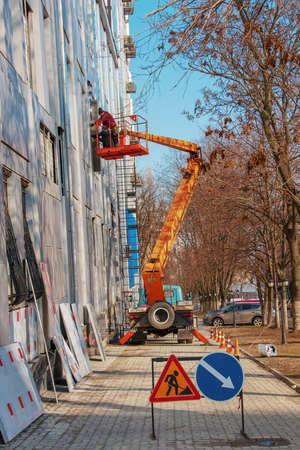Dnepropetrovsk, Ukraine - 02.09.2022: Builder in a crane basket repairs the coating of a metal structure on the wall of the facade of a building.のeditorial素材