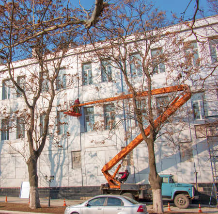 Dnepropetrovsk, Ukraine - 02.09.2022: Builder in a crane basket repairs the coating of a metal structure on the wall of the facade of a building.のeditorial素材
