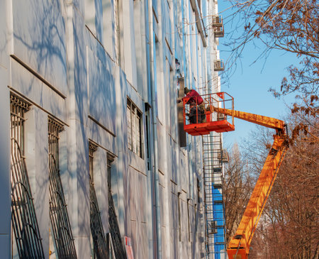 Dnepropetrovsk, Ukraine - 02.09.2022: Builder in a crane basket repairs the coating of a metal structure on the wall of the facade of a building.のeditorial素材