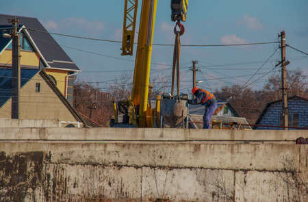 Dnepropetrovsk, Ukraine - 02.21.2022: Construction of a bypass road in the industrial area. Builder worker takes the load with concrete from the boom of the crane.のeditorial素材