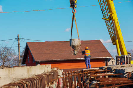 Dnepropetrovsk, Ukraine - 02.21.2022: Construction of a bypass road in the industrial area. Builder worker takes the load with concrete from the boom of the crane.のeditorial素材