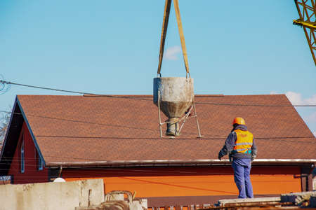 Construction of a bypass road in the industrial area. Builder worker takes the load with concrete from the boom of the crane.の写真素材