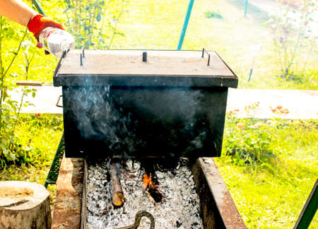 Smokehouse for hot smoking on fire. A man pours water into the shutter of a smokehouse.の写真素材