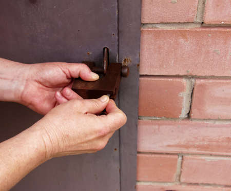 Women's hands open a rusty lock with keys. Lock on a metal door. security.の写真素材
