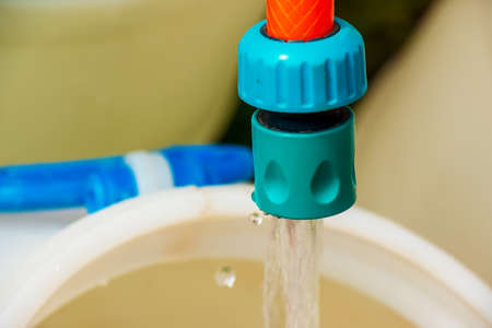 A jet of water from a hose fills a plastic barrel. background image. The concept of the drinking...