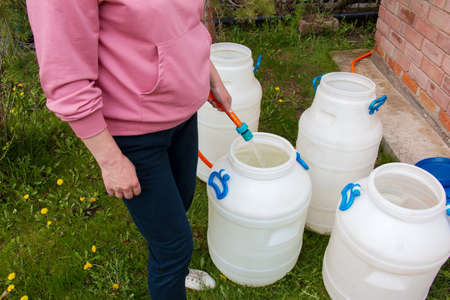 Woman fills a plastic barrel with water from a hose. The concept of the drinking water crisis in the...