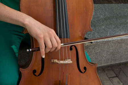 Detail of a man playing the wooden cello rubbing the strings with the bow to get the notes of a classical music piece.の写真素材
