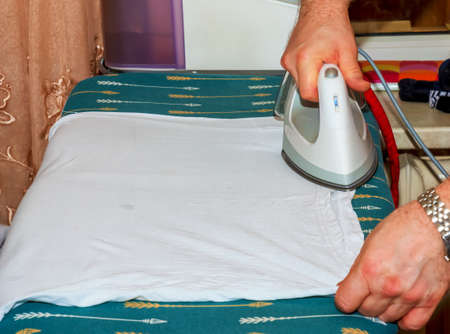A man irons clothes on an ironing board with a white iron. Housework and household concept. ironing...