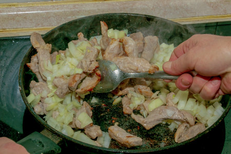 Pieces of pork and chopped white onion, fried in a hot pan with oil, close-up.の写真素材