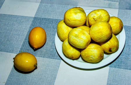 Lemons without zest on a white plate on the table. Two fresh lemons are on the table.