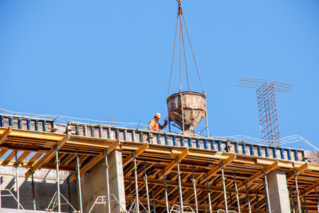 Dnipro, Ukraine - 02.15.2022: A crane lifts concrete for a modern metal-concrete structure of a residential building. Container with concrete against the blue sky.のeditorial素材