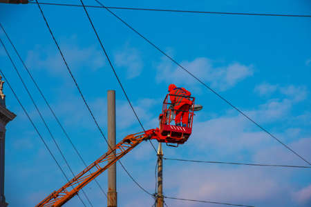 Electrician repairing wire of the power line with bucket hydraulic lifting platform on blue skyの写真素材