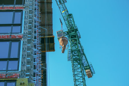 A crane lifts concrete for a modern metal-concrete structure of a residential building. Container with concrete against the blue sky.の写真素材