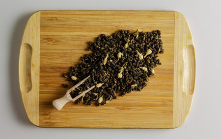 Green dry tea with jasmine flowers on a wooden board and a wooden spoon dispenser. Background and texture of dry tea.の写真素材