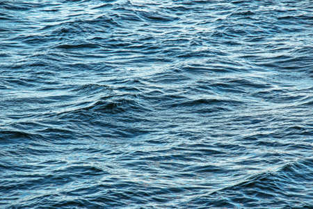 The background of the surface of the water of the river with small ripples and reflections of autumn...