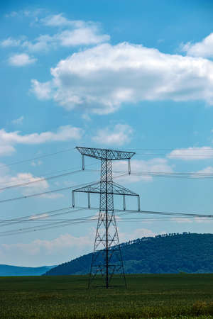 High voltage lines and power pylons in a green landscape on a sunny day with clouds in the blue sky.