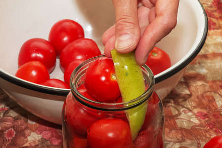 The process of preserving tomatoes for the winter. Female hands stack ripe red juicy tomatoes in glass jars.の写真素材