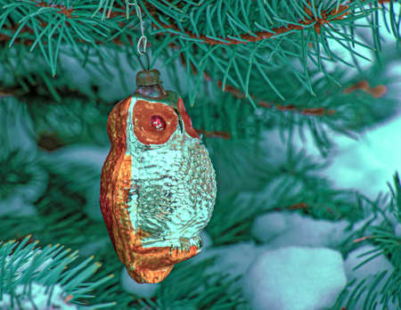 Christmas toy owl hangs on a snow-covered branch of a Christmas tree on a festive background of white snow bokeh with copy space. New Year, greeting and holiday card, banner.の写真素材