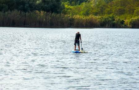 Dnipro, Ukraine - 08/09/2022: a sports man of advanced years rides a sapboard on the river. photo set. city water activities.のeditorial素材