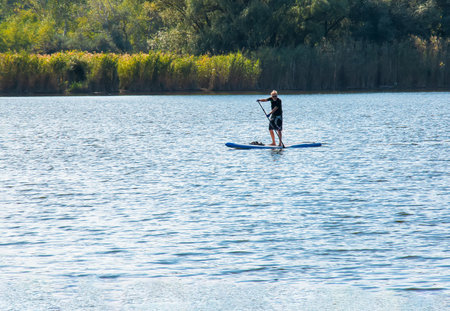 Dnipro, Ukraine - 08/09/2022: a sports man of advanced years rides a sapboard on the river. photo set. city water activities.のeditorial素材