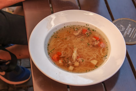 Bojnice, Slovakia - 11/06/2022: Soup with noodles and vegetables in a white plate on a wooden table.のeditorial素材