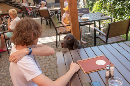 Bojnice, Slovakia - 06.11.2022: A young man sits at a table in a cafe and looks at his dog with pleasure.のeditorial素材