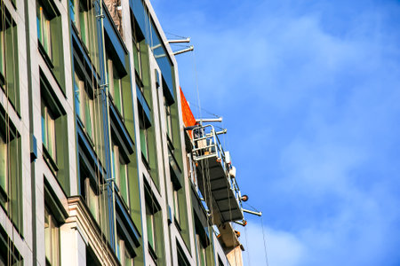 Suspended platform, construction cradle hanging on building. Installation and repair work. Building facades construction works. Facade of high-rise building under construction, finishing worksの写真素材