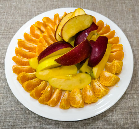 Peeled tangerines sliced and red and yellow apples cut into slices on a white plate. Healthy food concept.の写真素材
