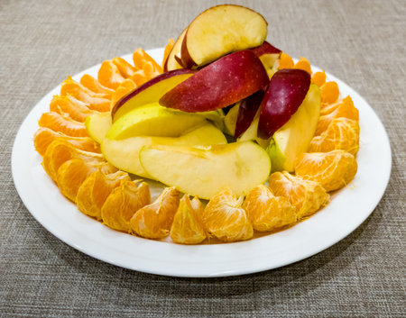 Peeled tangerines sliced and red and yellow apples cut into slices on a white plate. Healthy food concept.の写真素材