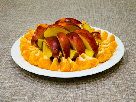 Peeled tangerines sliced and red and yellow apples cut into slices on a white plate. Healthy food concept.の写真素材