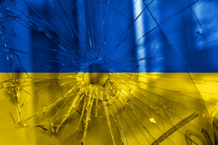 Bullet hole, cracks in the glass on a yellow-blue background. Ukraine flag on broken glass texture. Concept, Russian-Ukrainian war.の写真素材