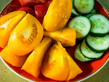 Close-up of slices of yellow and red tomatoes and cucumbers. Vegetables prepared for salad.の写真素材