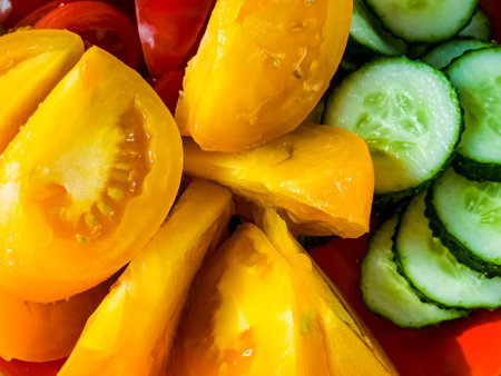 Close-up of slices of yellow and red tomatoes and cucumbers. Vegetables prepared for salad.の写真素材
